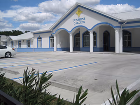 Sunshine Gardens building front with white-blue exterior and arched entryway.