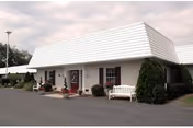 Exterior view of a single-story retirement community building with a white roof and benches.