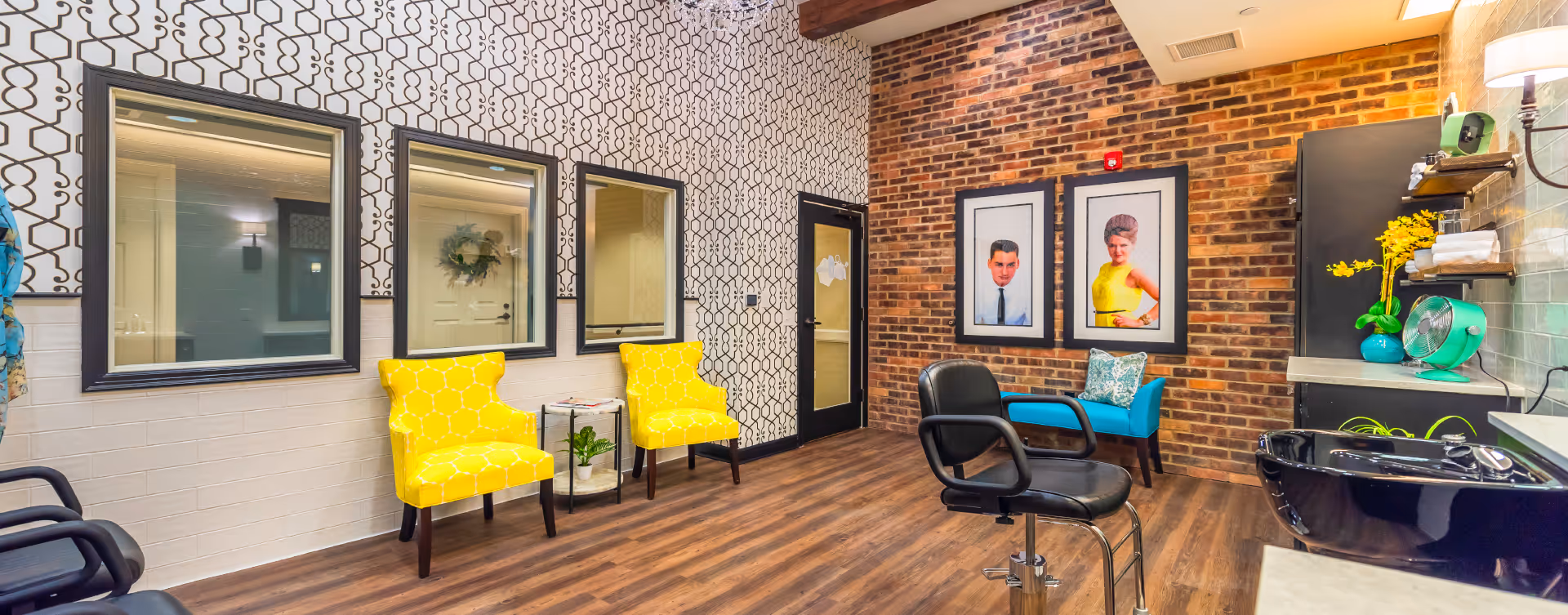 Bright salon-style interior with yellow accent chairs, styling stations, mirrors and an exposed brick accent wall.