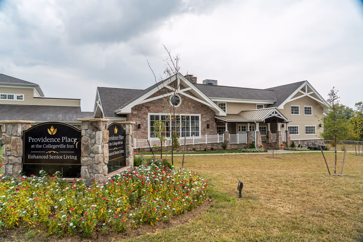 Front exterior of Providence Place Senior Living building with a landscaped sign and flowerbed in the foreground.
