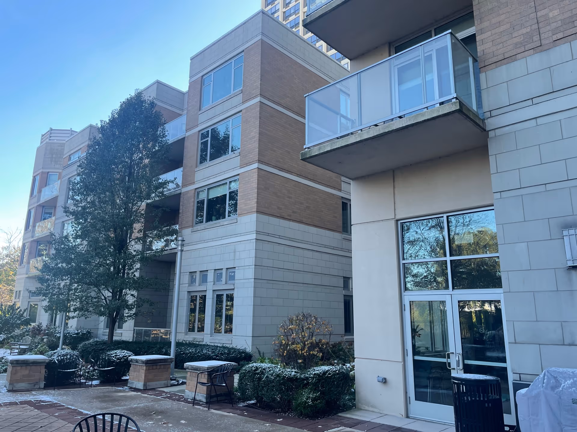 Exterior courtyard and entrance of a multi-story brick and stone senior living building with balconies, trees, and outdoor seating.
