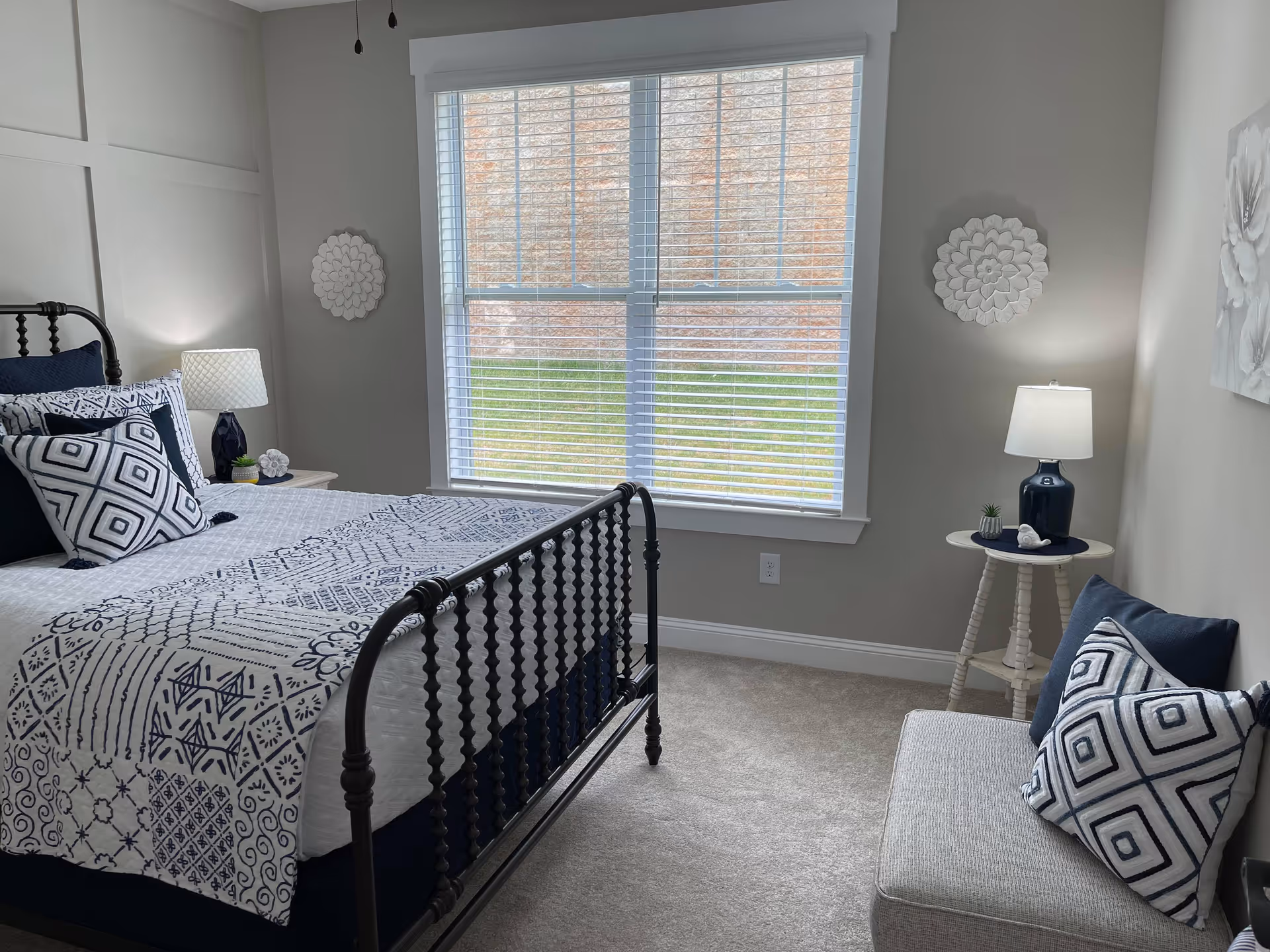 Neat bedroom with a black metal bed, blue-and-white patterned bedding, window with blinds, and bedside tables with lamps.