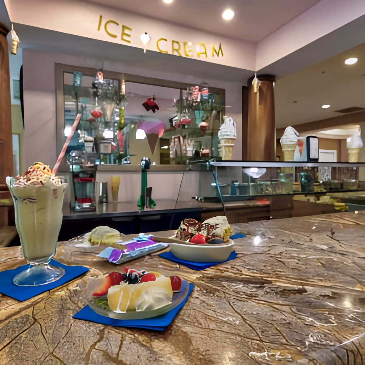 Marble countertop displaying ice cream desserts and a milkshake in front of a glass service counter under an "ICE CREAM" sign inside a dining area.