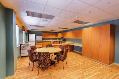 A communal dining area with a round table and patterned chairs beside a kitchen counter.