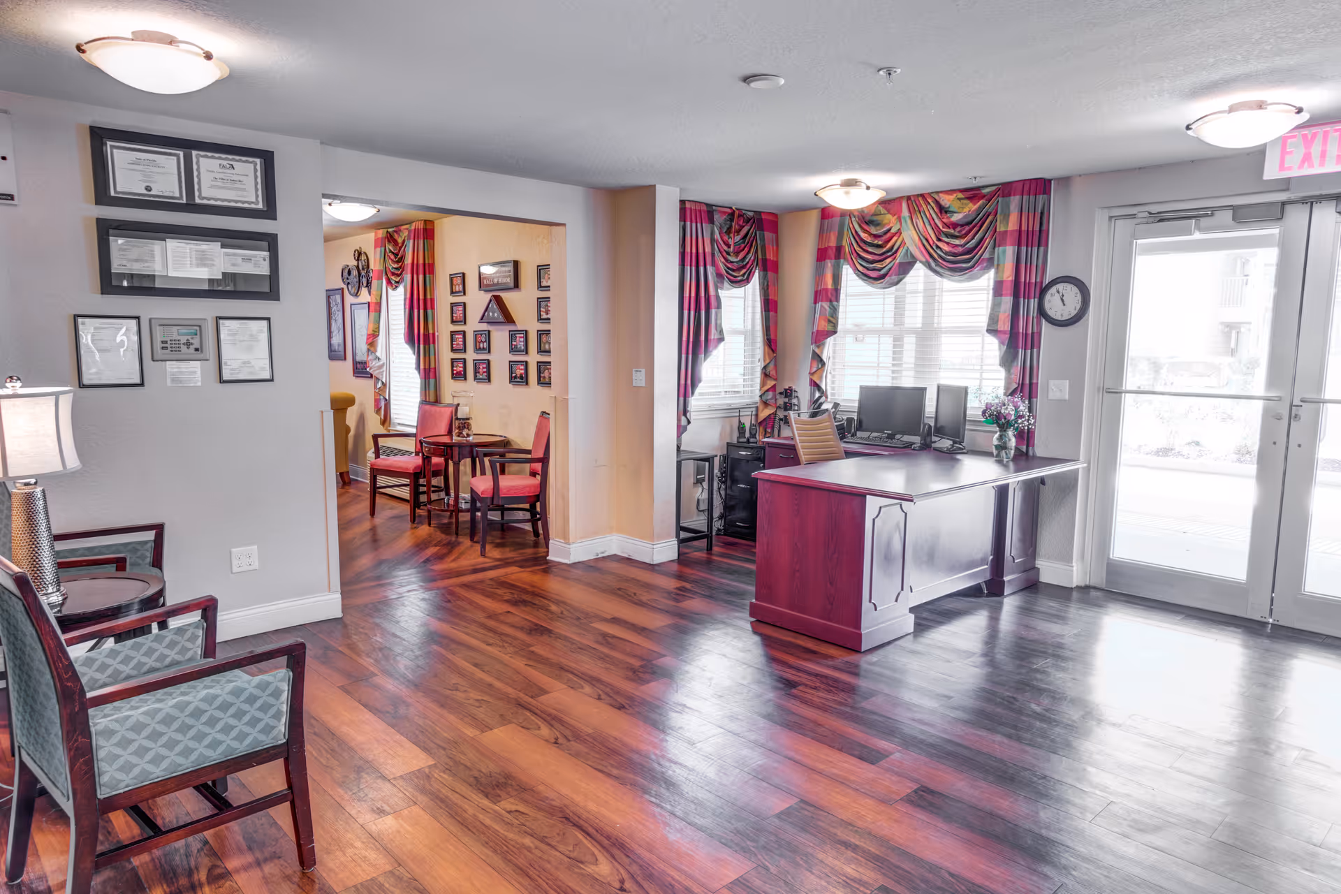 Reception lobby with a wooden desk, seating area, hardwood floors, colorful draped curtains, and framed certificates on the wall.