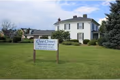 A white two-story senior living building sits on a green lawn with a sign in front.