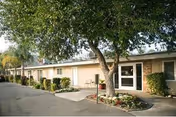 Single-story brick care facility front with a walkway, landscaped beds, and a tree near the entrance.
