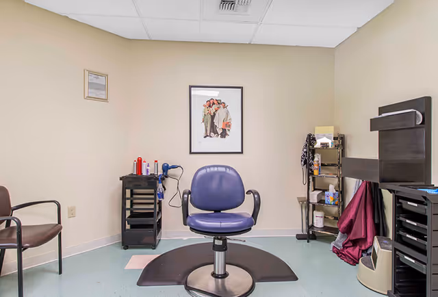 Small salon/styling room with a central purple salon chair, styling cart with hair tools, and framed art on the wall.