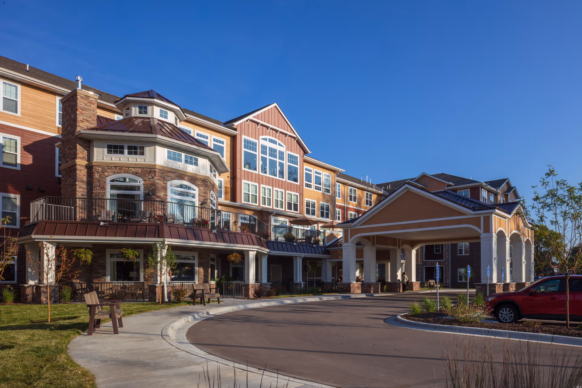 Front exterior of a multi-story senior living building with a covered porte-cochere, balconies, and a circular driveway.