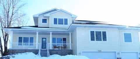 Light-colored two-story senior living facility with a front porch, snow on the ground, and a garage.