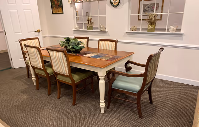 Rectangular wooden dining table with six upholstered chairs, a plant centerpiece, and decorative wall niches.