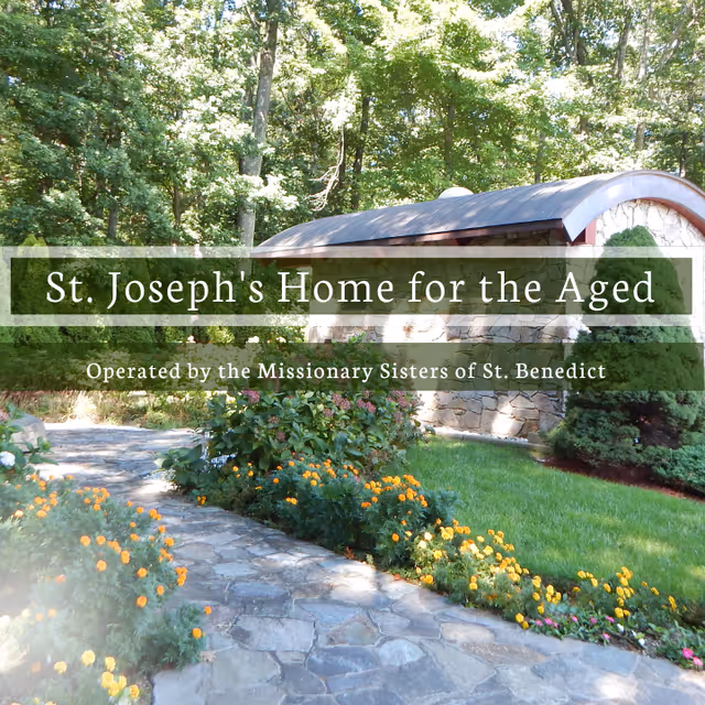 A stone pathway bordered by vibrant yellow and orange flowers leads through a lush green garden with trees and shrubs. In the background, there is a stone building with a curved roof. Overlaid text reads 'St. Joseph's Home for the Aged, Operated by the Missionary Sisters of St. Benedict.'
