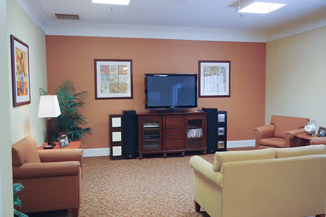 Cozy communal living room with sofa and armchairs facing a TV on a wooden media console against an orange accent wall.