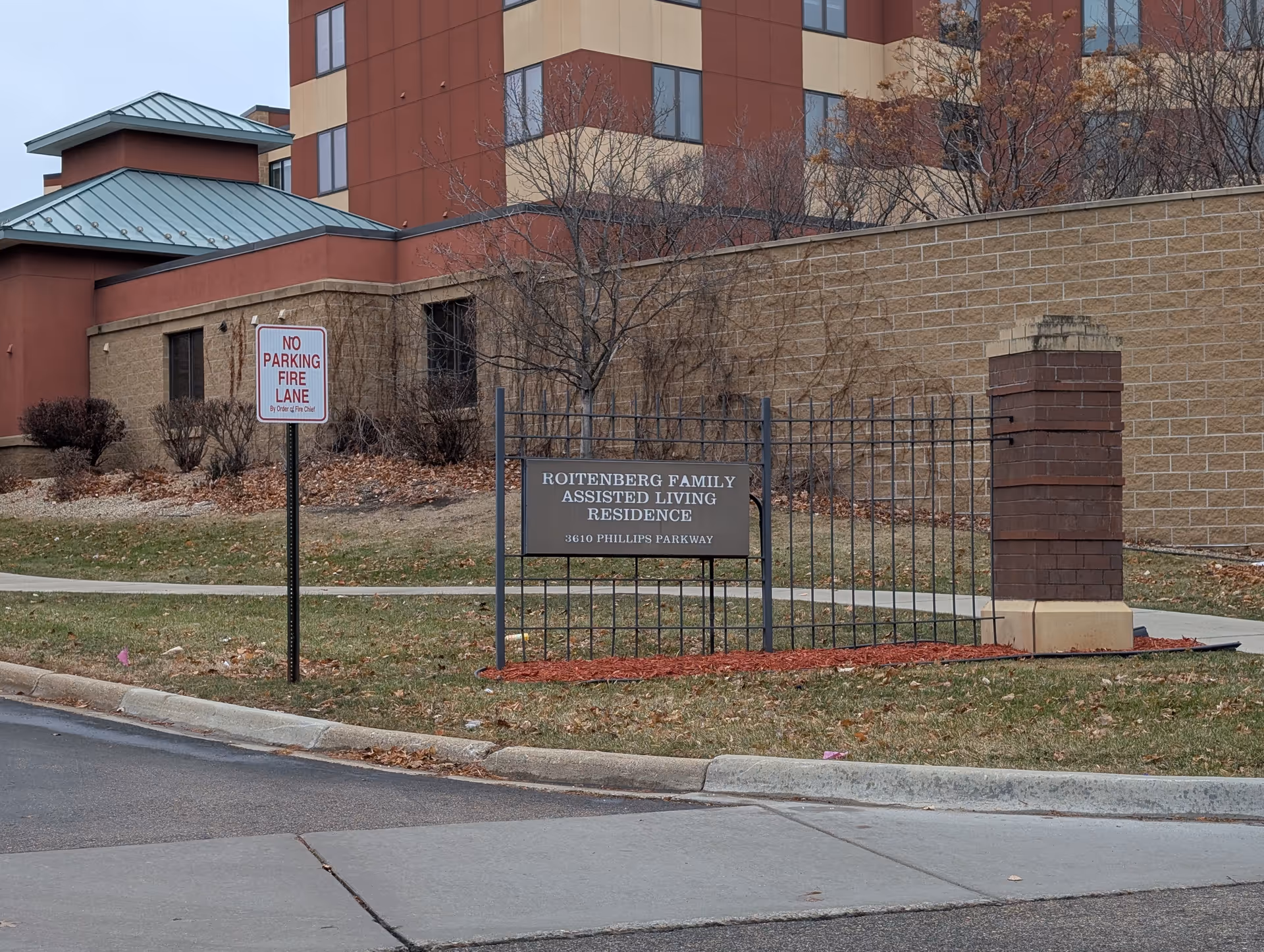 Exterior view of an assisted living residence entrance sign and building façade with a 'No Parking Fire Lane' sign nearby.