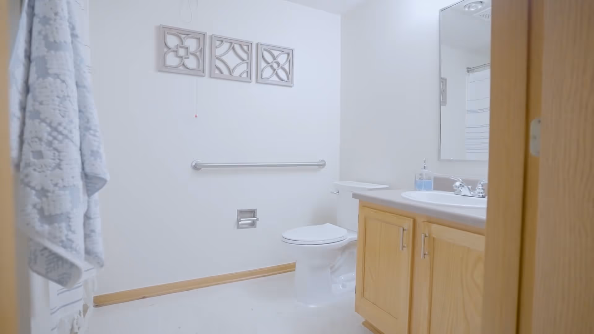 Bright bathroom with a toilet, vanity sink, grab bar, towel, and decorative wall panels.