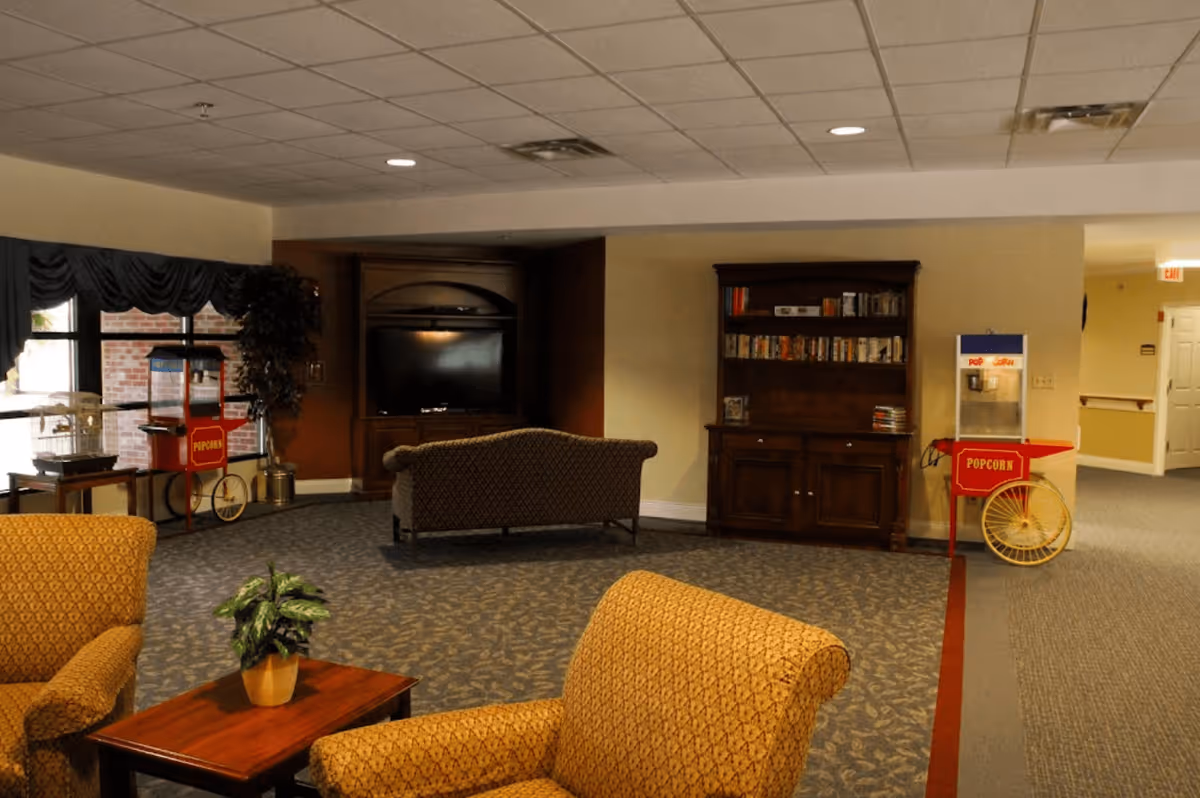 Communal lounge with upholstered chairs, a TV cabinet, bookshelf, and two popcorn carts.