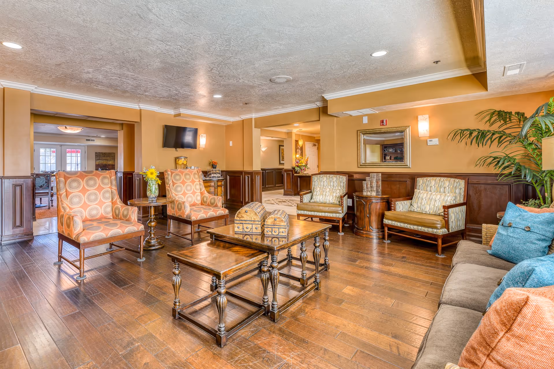 Comfortable lobby seating area with patterned armchairs, coffee tables, a TV, and warm wood-paneled decor.