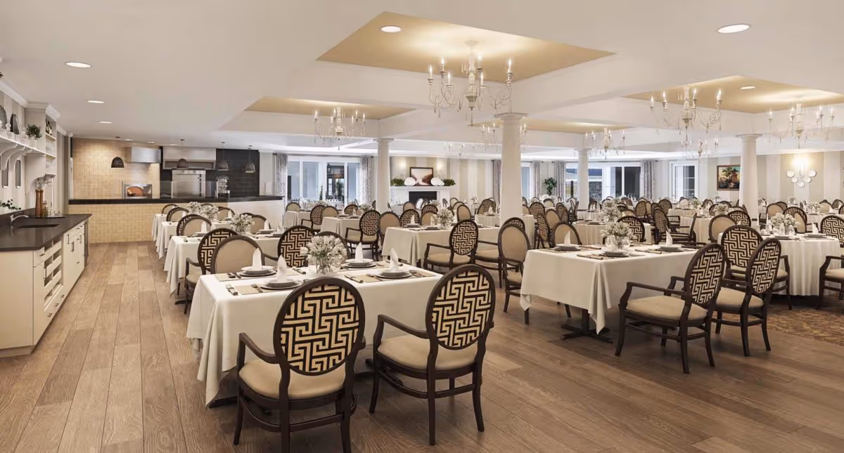 Spacious elegant dining room with many tables set with white tablecloths and patterned chairs.