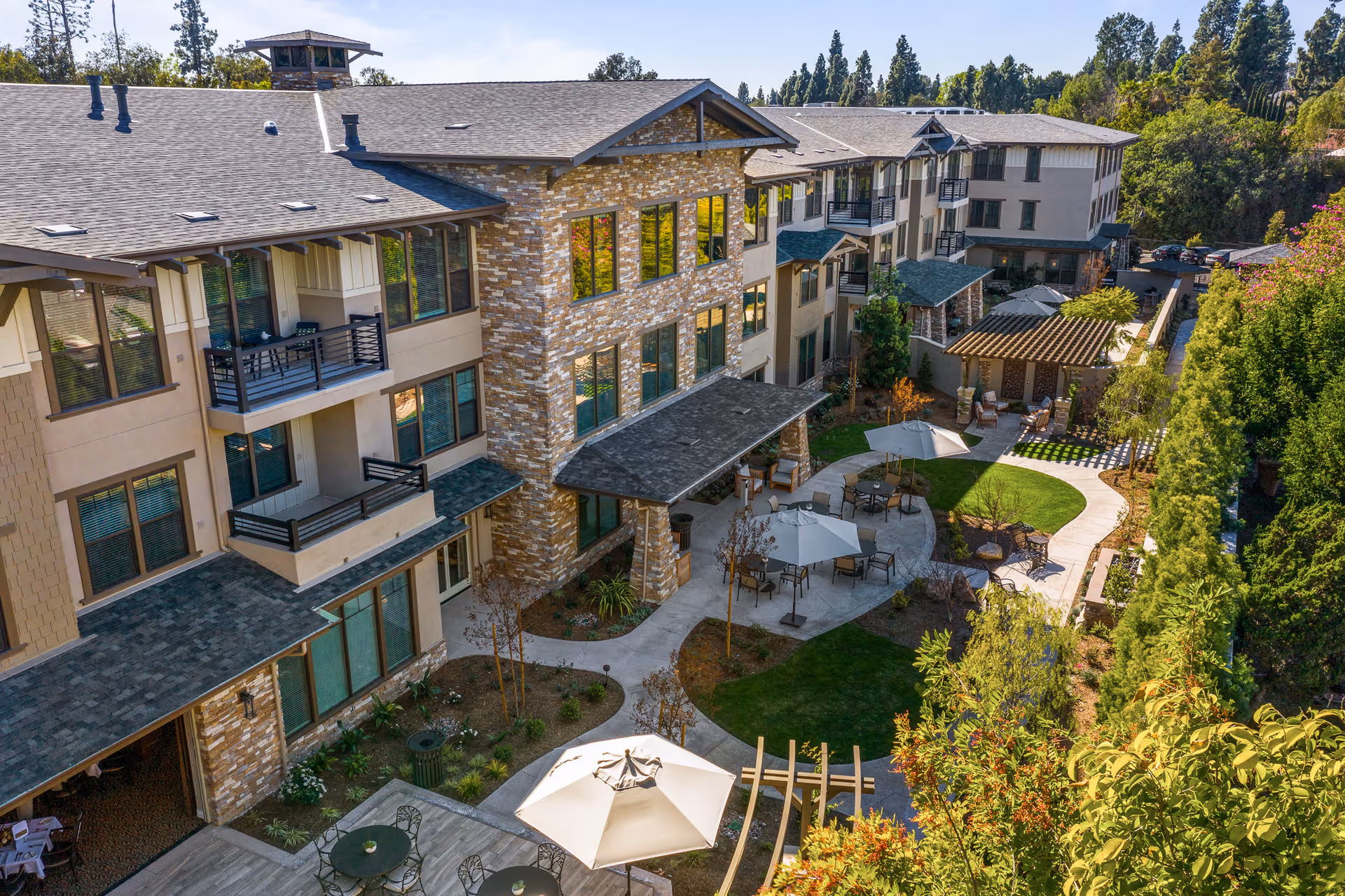 Aerial view of a multi-story senior living building with a landscaped courtyard, walkways and outdoor seating with umbrellas.