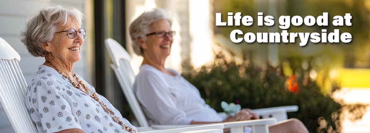 Two elderly women sitting and smiling on white rocking chairs outdoors with greenery in the background. Text on the image reads 'Life is good at Countryside'.