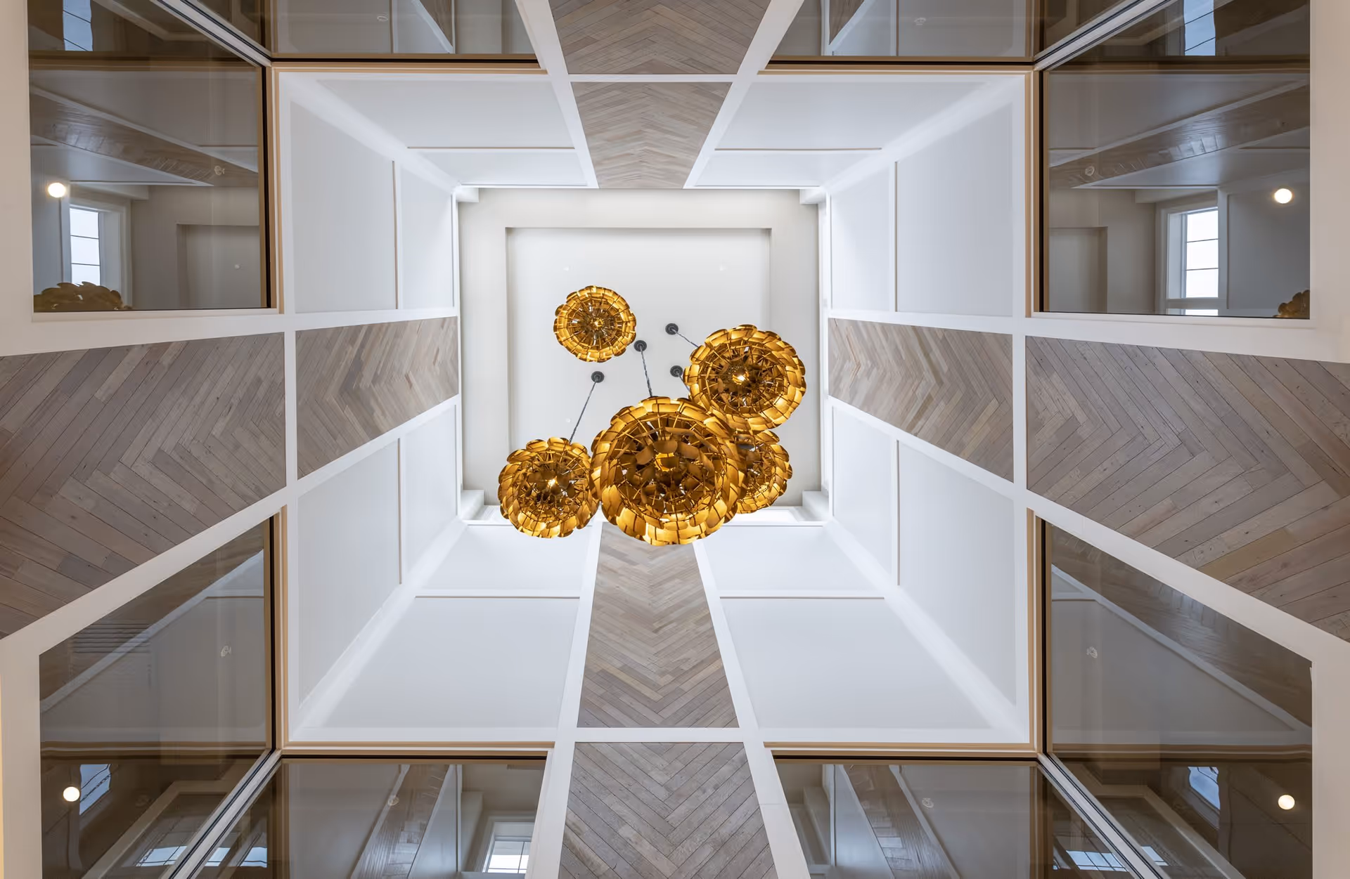 View looking up at a modern ceiling with white paneling and wood accents arranged in a chevron pattern, featuring a cluster of five decorative golden pendant lights hanging from the center.