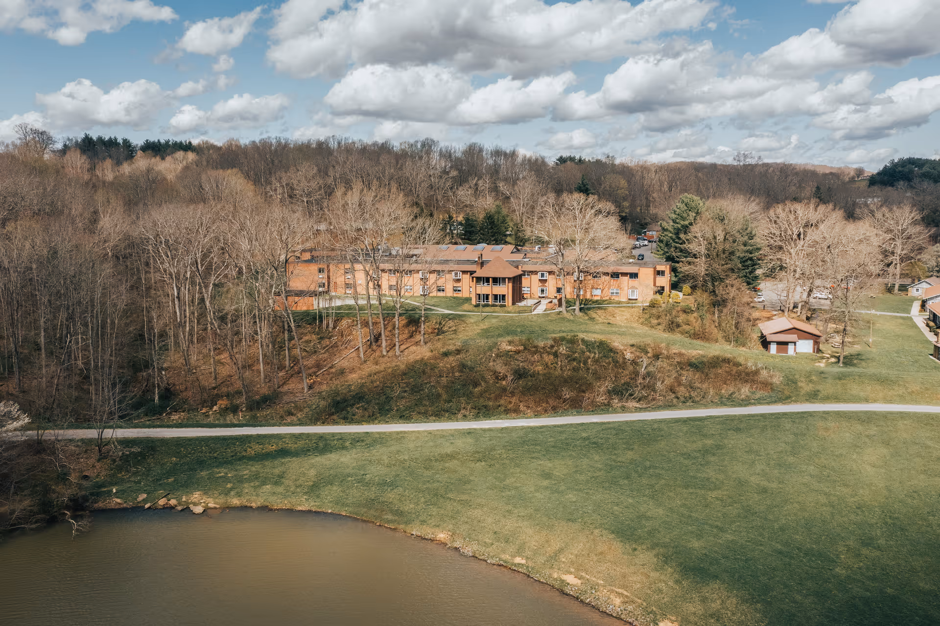 Aerial view of Glenwood Healthcare Center's brick building on a grassy hill beside a pond and surrounded by trees.