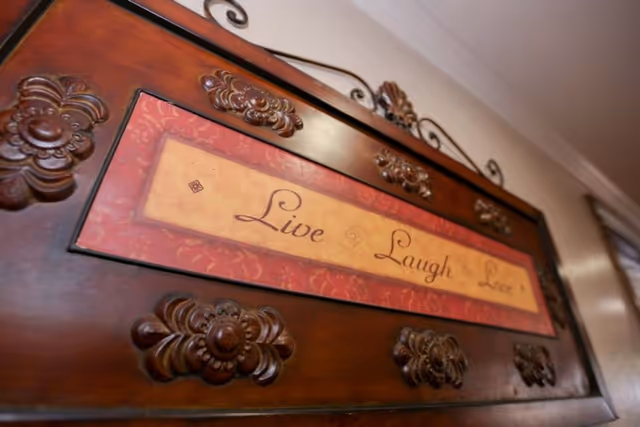 A decorative wooden plaque with ornate carvings and a metal hanger, featuring the inspirational words 'Live Laugh Love' in elegant script.
