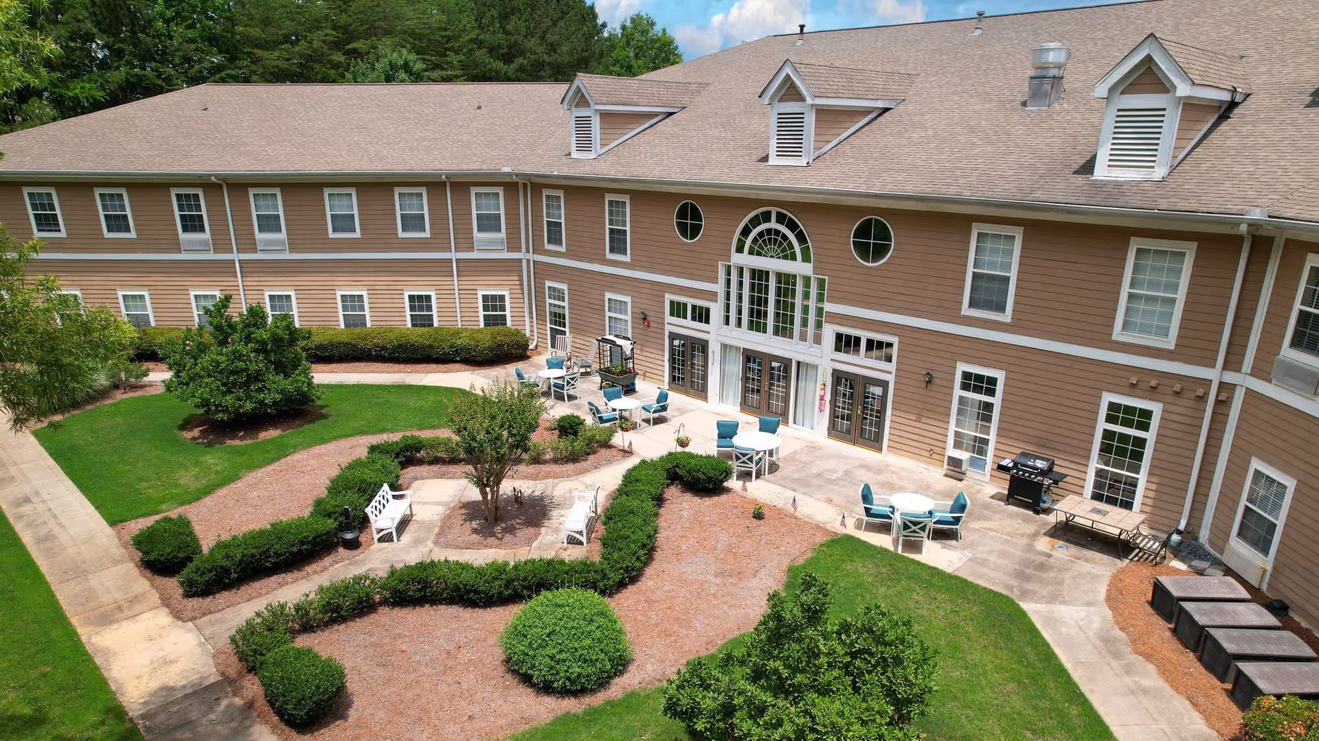 Aerial view of a landscaped courtyard with pathways, patio seating, and the two-story exterior of a senior living building.