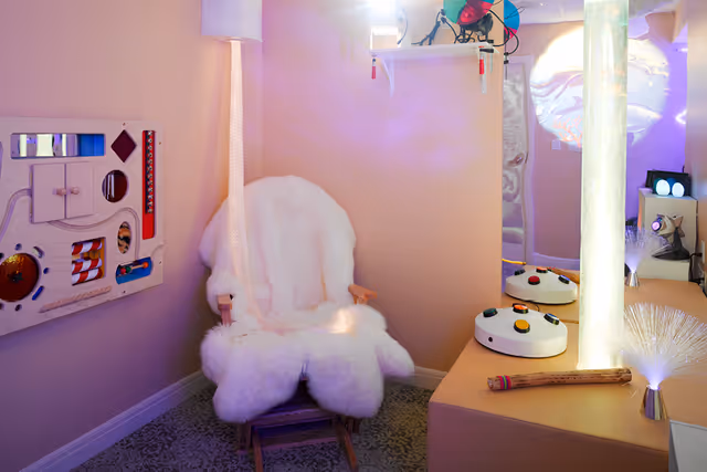 Cozy sensory room featuring a fluffy white armchair, illuminated fiber-optic lights, and interactive sensory panels.