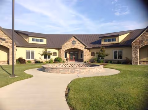 Front view of The Raymond House senior living facility with a circular stone fountain
