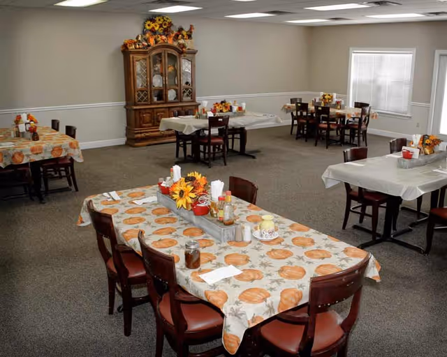 A dining room with tables covered in pumpkin-themed tablecloths and floral centerpieces.