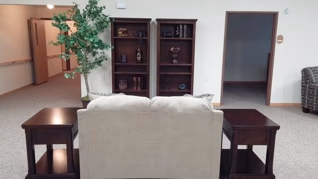 A small common living area with a beige sofa facing two wooden bookshelves, dark end tables, and a potted plant.