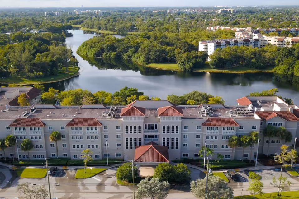 Aerial view of a multi-story building with red tile roofs overlooking a lake and surrounding greenery.