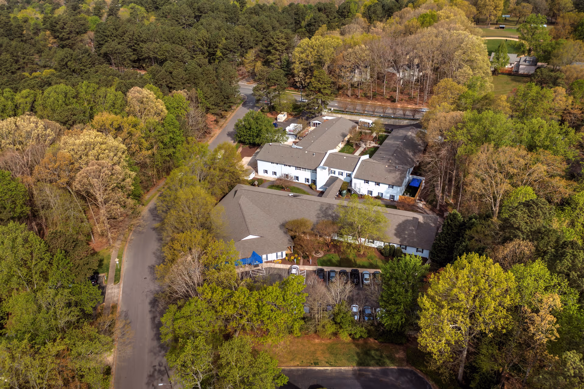 Aerial view of TerraBella Northridge senior living facility surrounded by dense trees and greenery, showing multiple connected buildings with parking spaces and roads nearby.