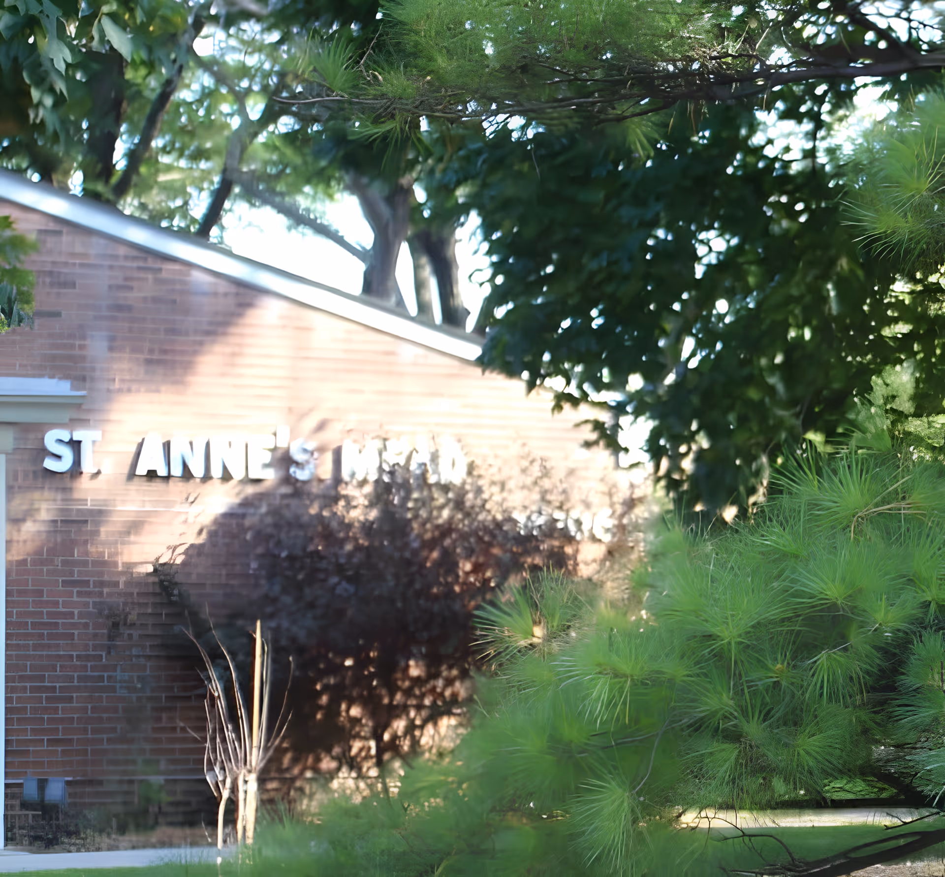 Brick building facade with a partial "ST. ANNE'S" sign partly obscured by trees and green foliage.