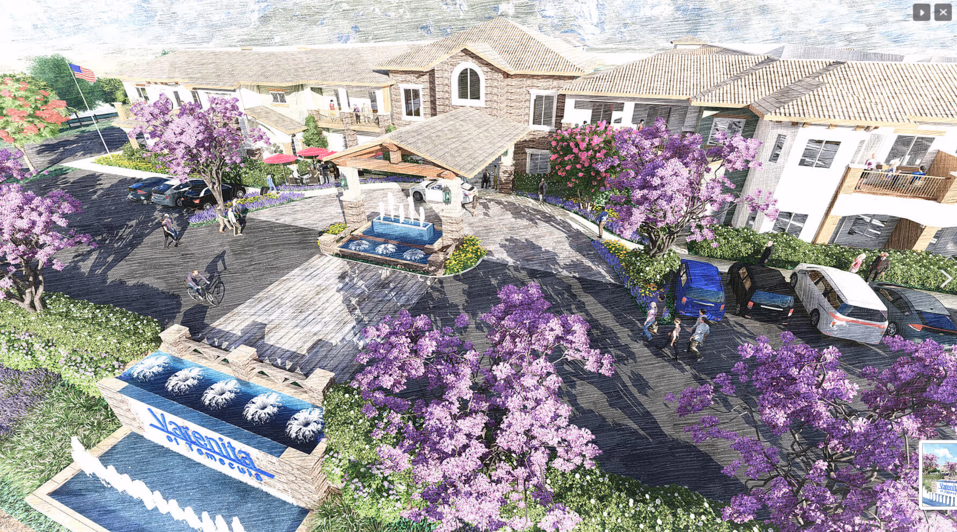 Aerial view of the entrance to Varenita of Temecula senior living facility showing a two-story building with balconies, a driveway with parked cars, a covered drop-off area, and landscaped grounds with purple flowering trees and a water fountain sign displaying the facility's name.