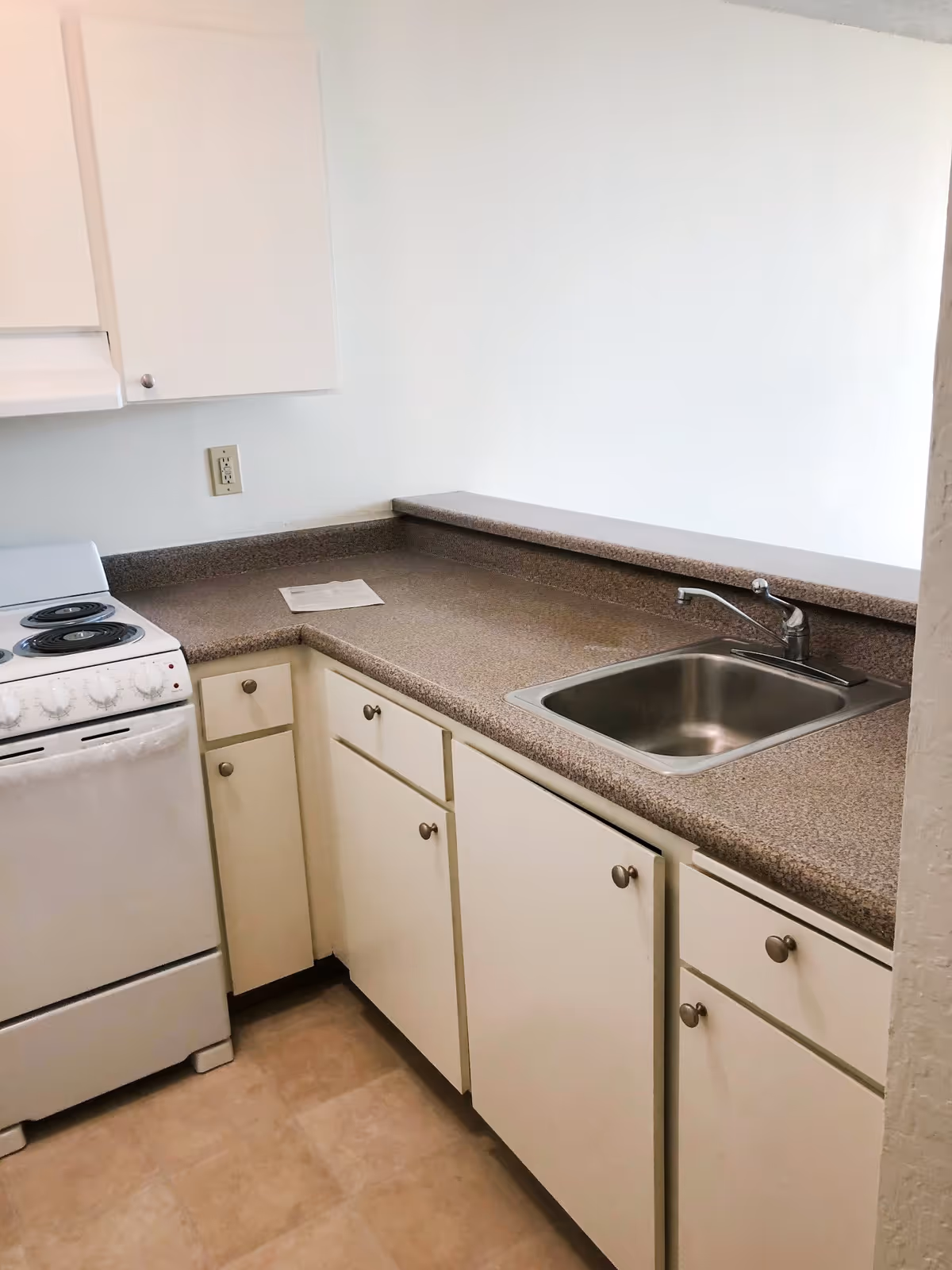 Compact kitchen with white cabinets, laminate countertops, a stainless sink and an electric stove.
