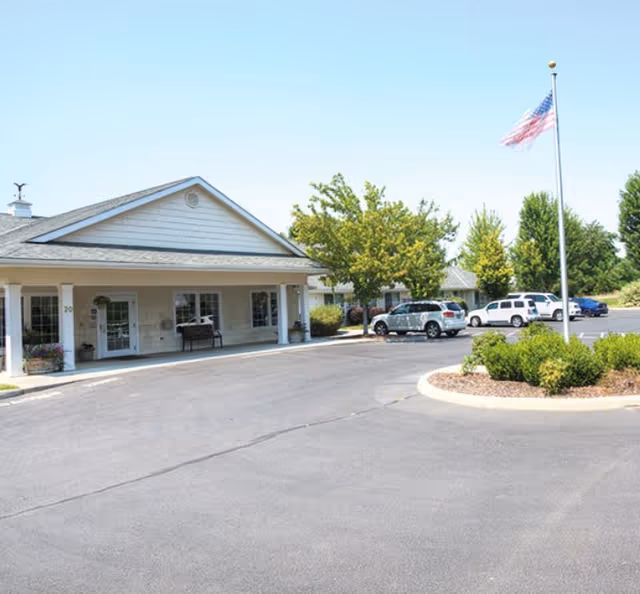 Exterior view of Eagle Springs Memory Care facility with entrance, cars, and flagpole.