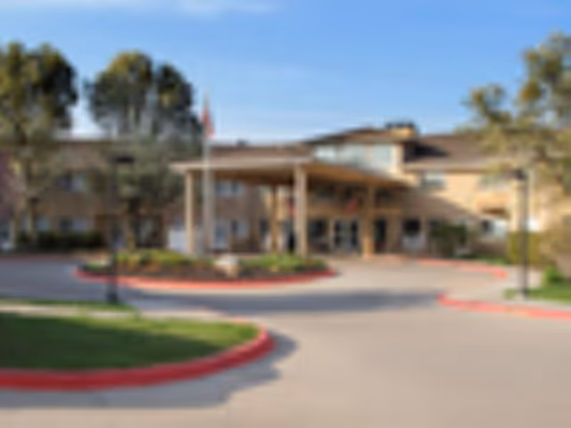 Front entrance of a two-story residential building with a covered porte-cochere, circular driveway, and landscaped islands.