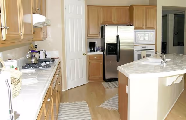 Bright kitchen with a center island, stainless steel refrigerator, wooden cabinets, and tiled countertops.