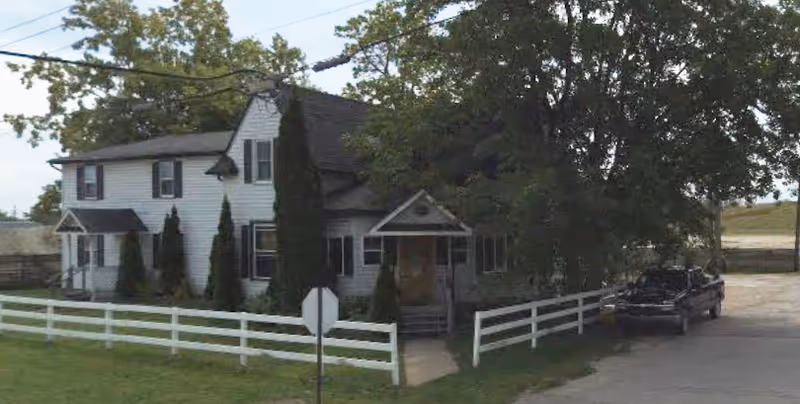 Front exterior of a two-story white house with a white fence, trees, and a parked truck.