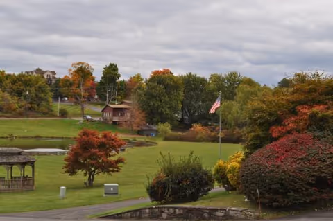 Well-kept lawn with gazebo, fall foliage, and a flag near the Valley Vista Assisted Living building.