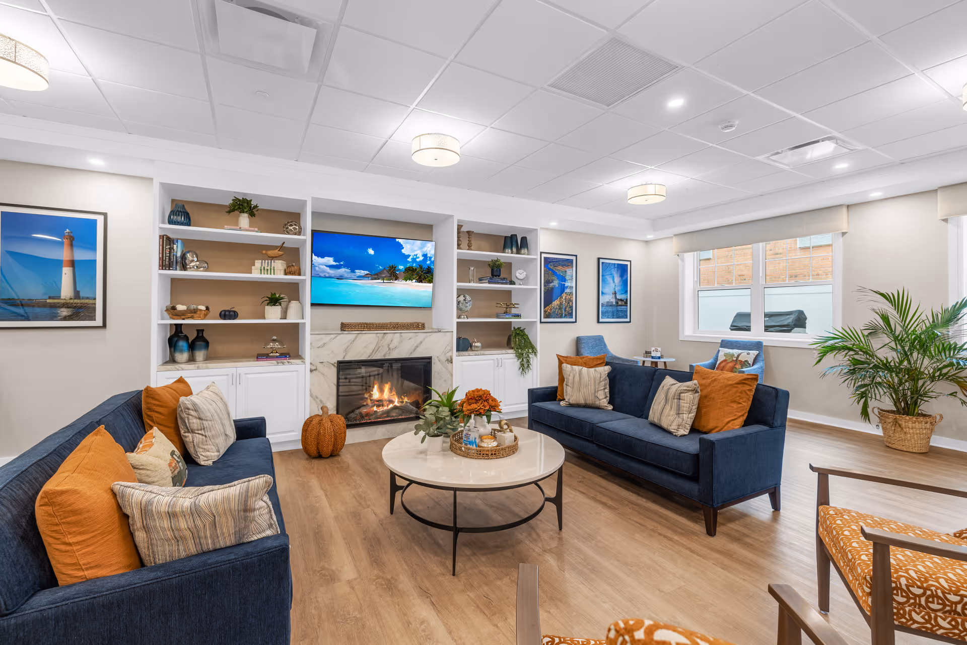 Bright community living room with two navy sofas facing a fireplace and TV, built-in shelves, coffee table and decorative accents.