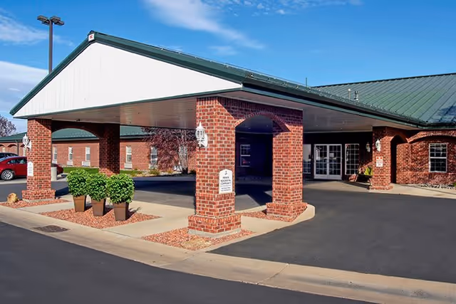Front entrance of a brick senior living building with a covered drive-through portico and green metal roof.