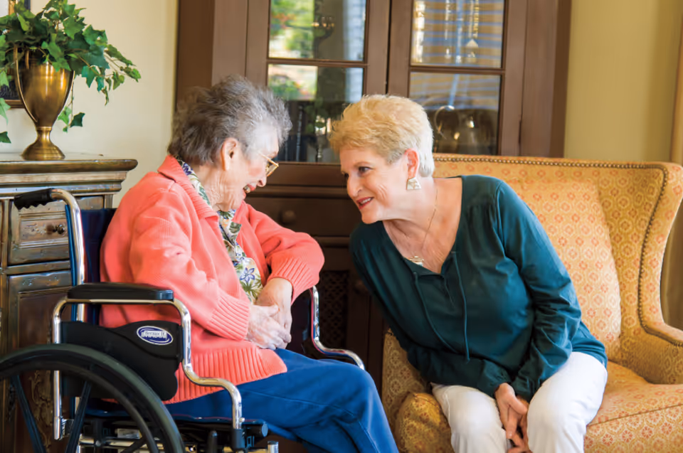 A caregiver interacts warmly with a resident in a senior living facility's cozy interior.