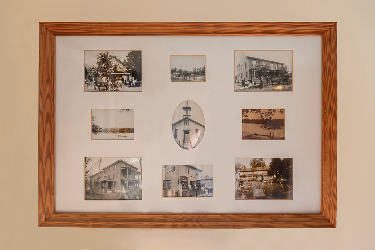 Wood-framed collage of vintage black-and-white photographs mounted on a beige wall.