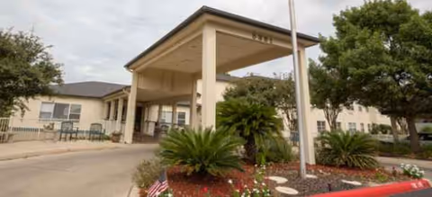 Front entrance of a senior living building with a covered drop-off and landscaping.