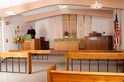 Chapel interior of a senior living facility with pews, pulpit, altar, and cross.