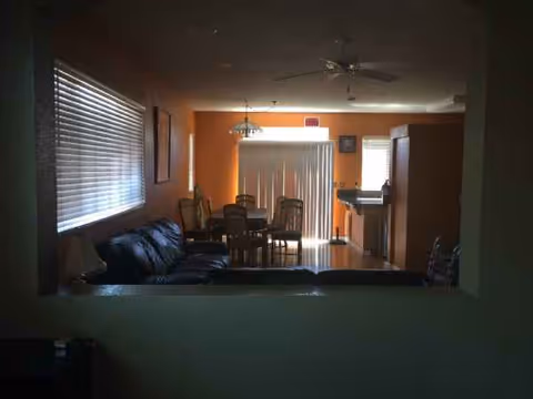 Living room with orange walls, sofa, dining table, and blinds in a senior home.