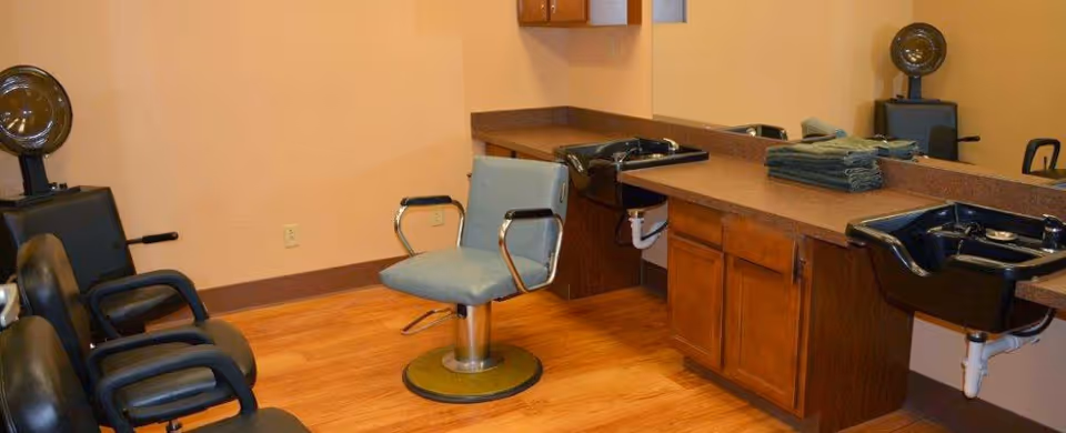 Salon-style room with styling chairs, hair-washing sinks, a long countertop and mirror with folded towels.